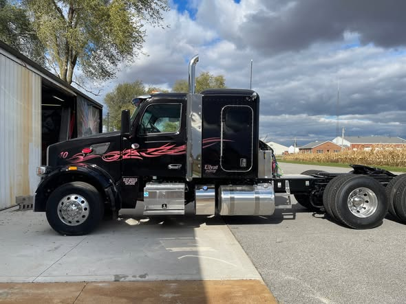 Black Ulyat Trucking Peterbilt semi with pink flame graphics parked next to the shop in Remington, Indiana