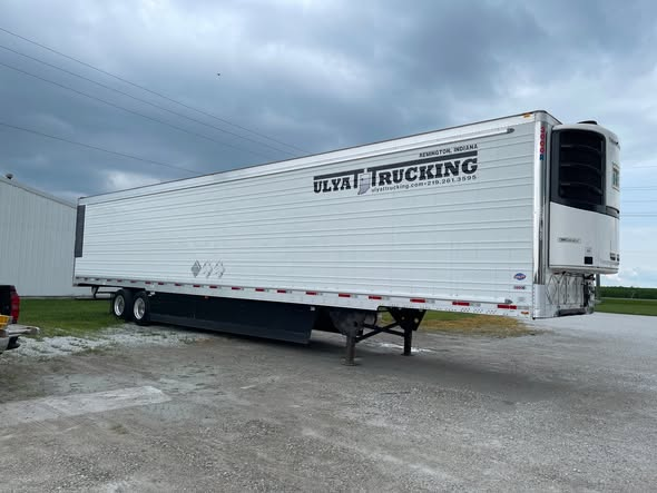 White refrigerated Ulyat Trucking semi-trailer parked on a gravel lot